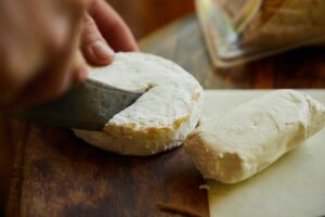 Rustic close-up of cheese wheel being cut with a knife on a wooden board.